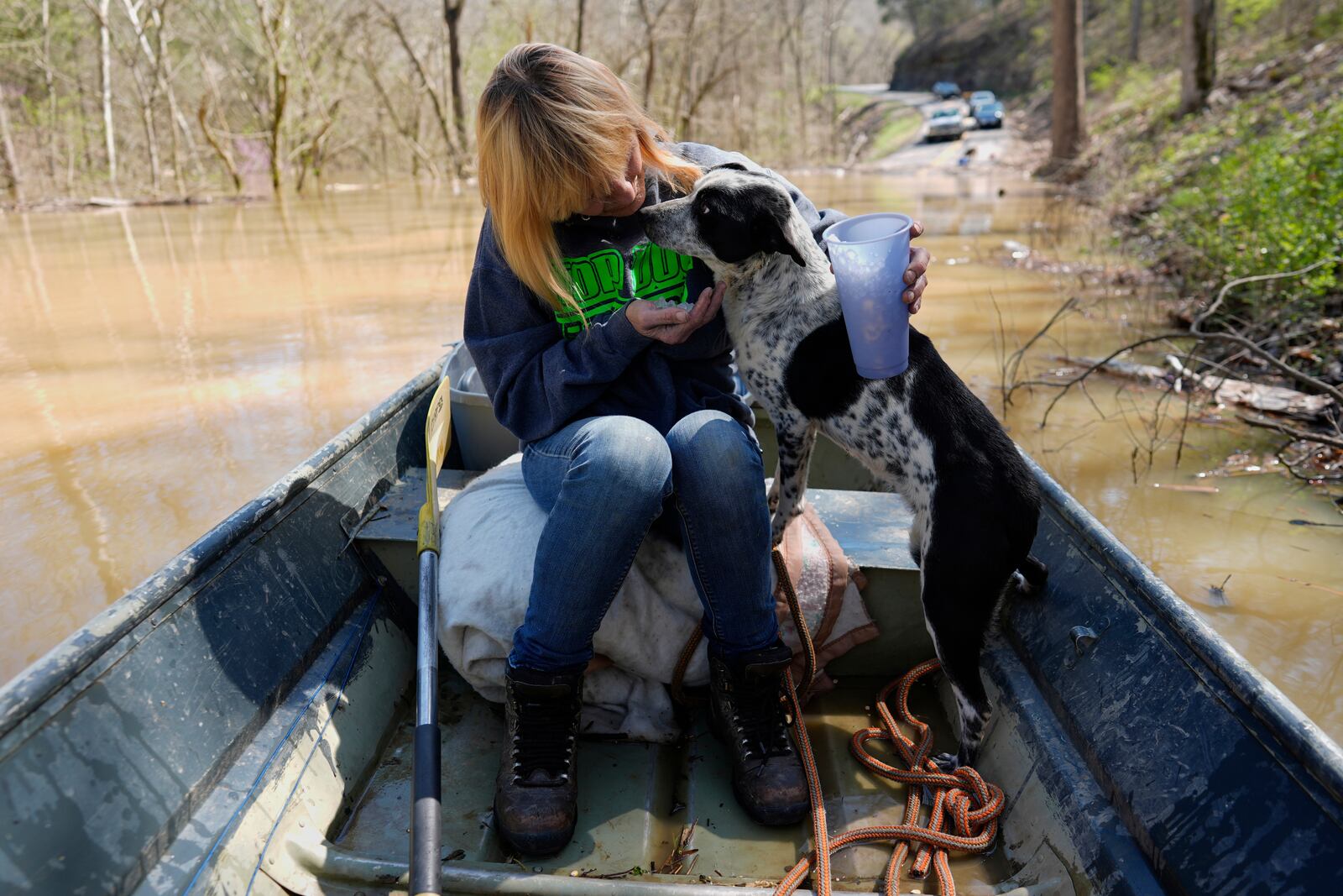 Wanona Harp offers a stranded dog some ice chips after coaxing it into a boat in Lockport, Ky., flooded by the Kentucky River, Tuesday, April 8, 2025. (AP Photo/Carolyn Kaster)