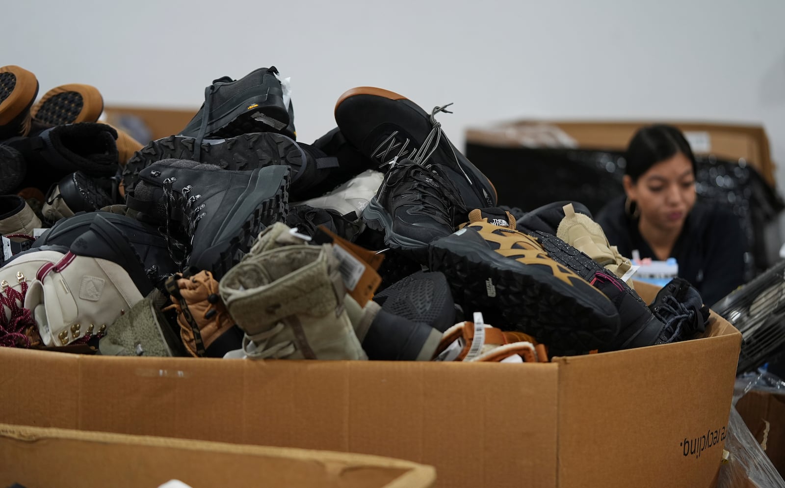 People work amid boxes of returned or overstocked clothing, shoes, boots, coats, packs and other items in a warehouse where the goods are cleaned or repaired before they are marketed on resale platforms in Englewood, Colo., on Thursday, April 17, 2025. (AP Photo/David Zalubowski)
