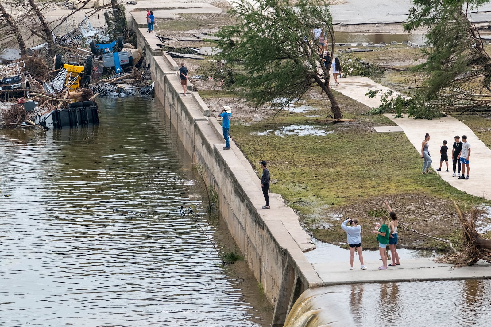 Onlookers walk along the banks of the Guadalupe River in Louise Hays Park, Saturday, July 5, 2025, in Kerrville, Texas. (AP Photo/Rodolfo Gonzalez)