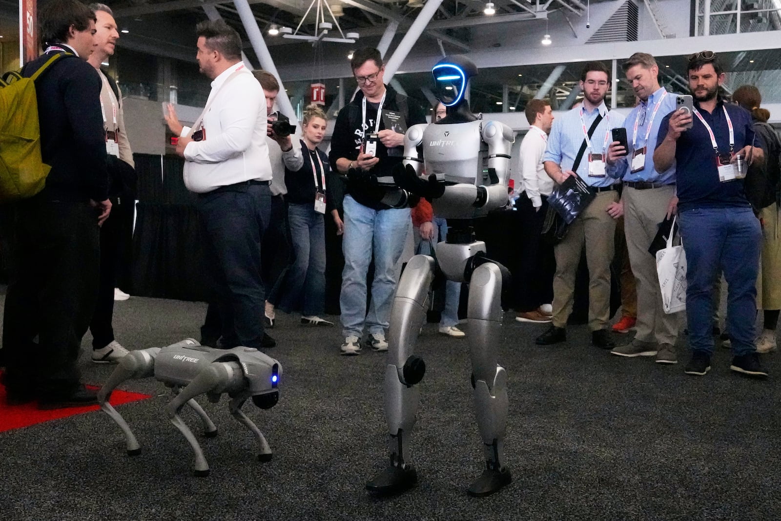 A human-like Unitree robot, right, passes out company brochures to convention guest, with a dog-like Unitree robot at its side, at the Robotics Summit & Expo, Wednesday, April 30, 2025, in Boston. (AP Photo/Charles Krupa)