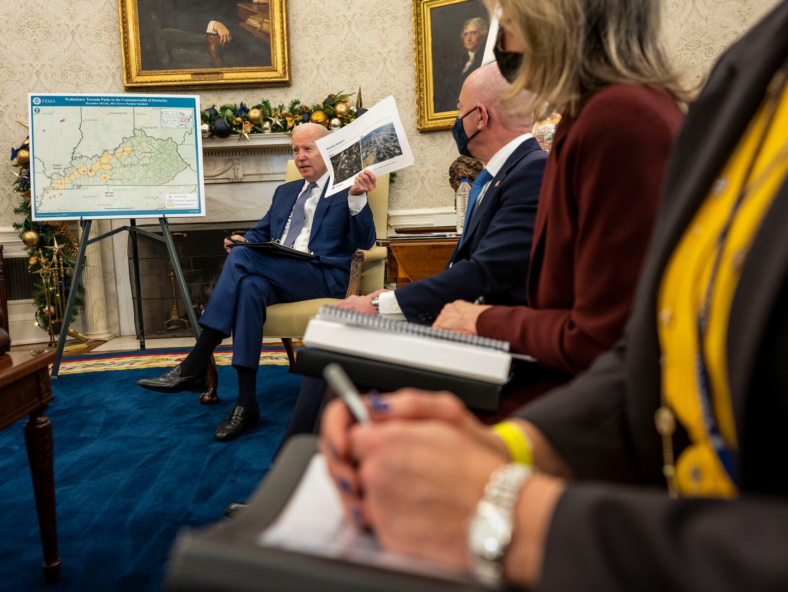 President Joe Biden holds photos of Mayfield, Ky., in the Oval Office of the White House in Washington on Monday, Dec. 13, 2021, as he speaks about the Federal response to the tornadoes that impacted multiple states. After grimly fluctuating death tolls since Friday’s devastating swarm of tornadoes, Gov. Andy Beshear of Kentucky said on Monday that there were 64 confirmed deaths in the state, though he expected that number to rise as crews continued to search through the ruins. (Doug Mills/The New York Times)