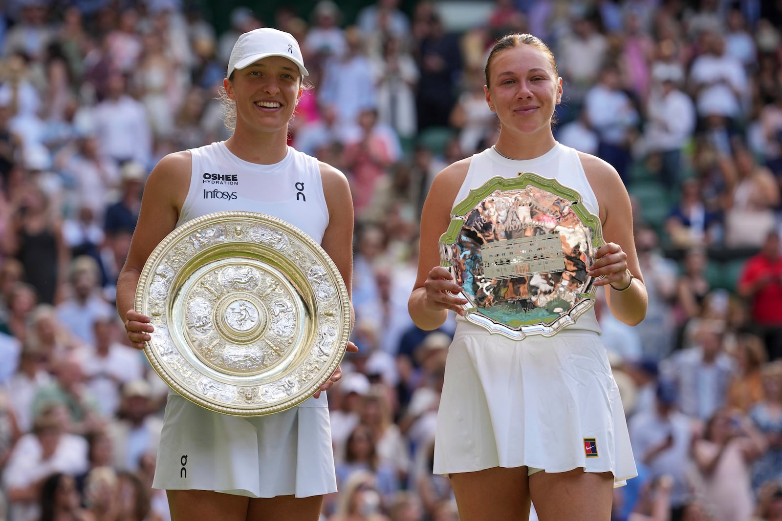 Poland's Iga Swiatek, left, celebrates with the trophy after beating Amanda Anisimova of the U.S., right, to win the women's singles final at the Wimbledon Tennis Championships in London, Saturday, July 12, 2025. (AP Photo/Kin Cheung)