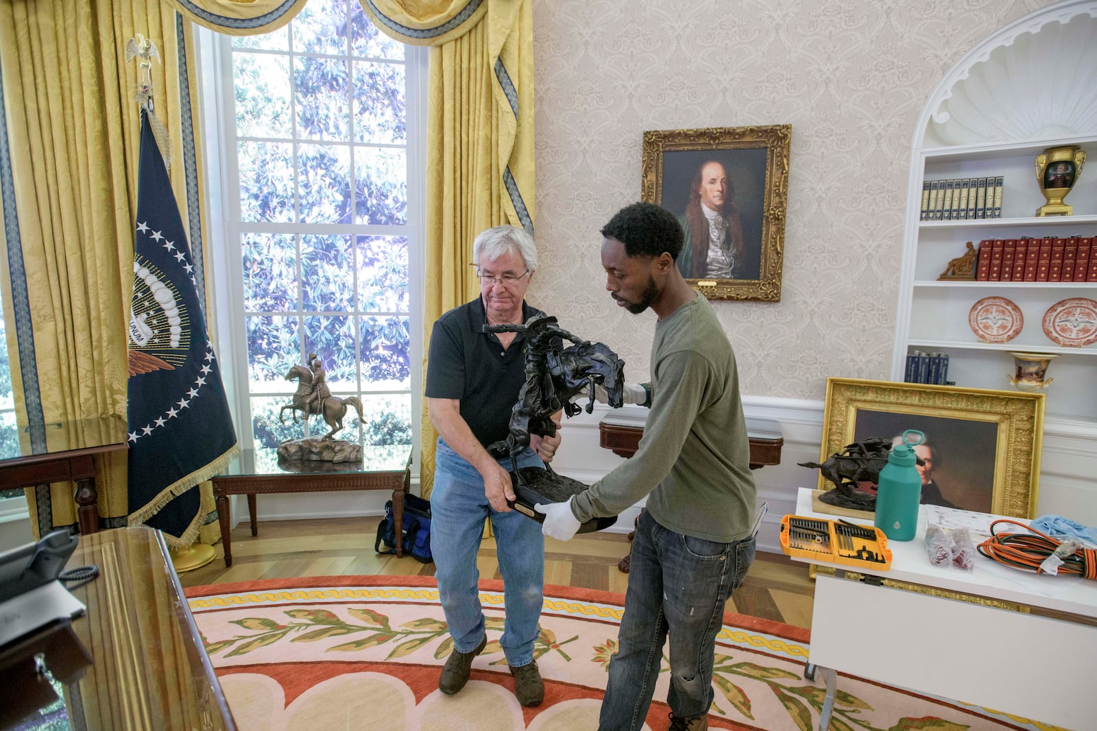 Tim Boyd, left, and Melvin Dorsey carry the "Bronco Buster" statue to the Resolute desk during work to transition a replica of the White House Oval Office from the days of former President Joe Biden with President Donald Trump's decor, at the White House Historical Association in Washington, Wednesday, July 23, 2025. (AP Photo/Rod Lamkey, Jr.)