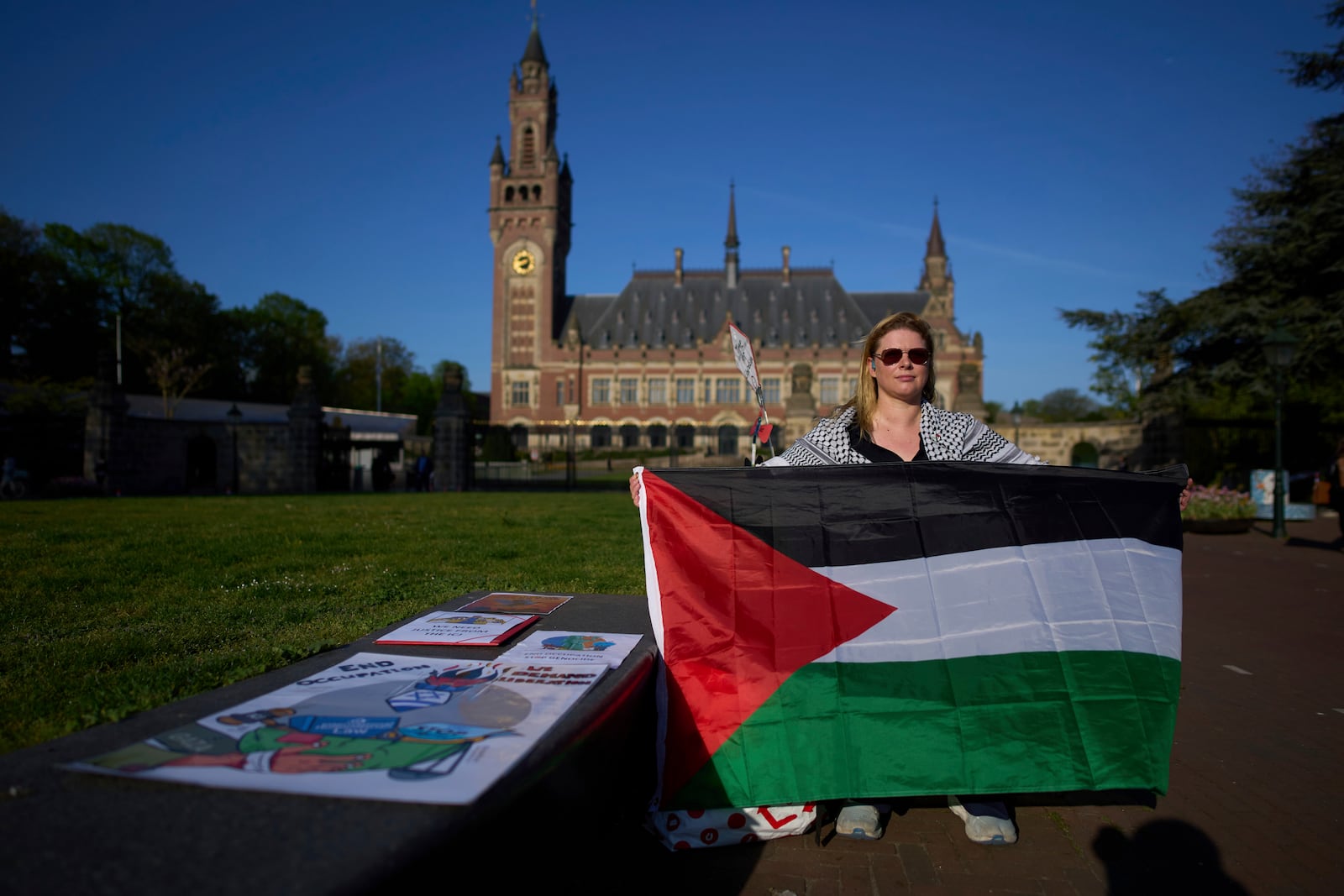 A protestor with a Palestinian flag waits for others to arrive at the International Court of Justice which opens hearings into a United Nations request for an advisory opinion on Israel's obligations to allow humanitarian assistance in Gaza and the West Bank, in The Hague, Netherlands, Monday, April 28, 2025. (AP Photo/Peter Dejong)