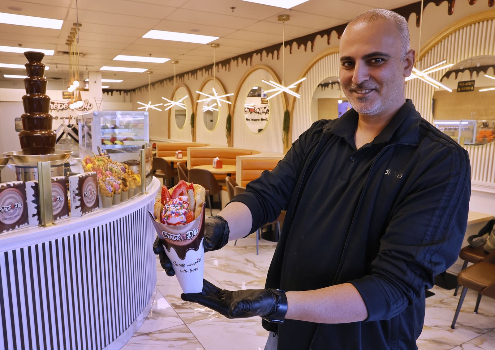 Crêpe N Dip on Tylers Place Blvd. in West Chester Township serves a variety of sweet treats including bubble waffles with gelato, fruit filled crepes, fruit cakes, coffee, shakes and more. Co-owner Moutazz Abdulhadi shows off a bubble waffle vone. NICK GRAHAM/STAFF