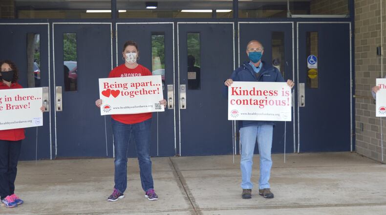 Volunteers from the Coalition for a Healthy Community, Oxford Ohio Area stand in the entryway at Talawanda Middle School May 20 displaying the four signs with messages the mental health workgroup is distributing around the area to promote positive feelings and to offer telehealth mental health services. CONTRIBUTED/BOB RATTERMAN