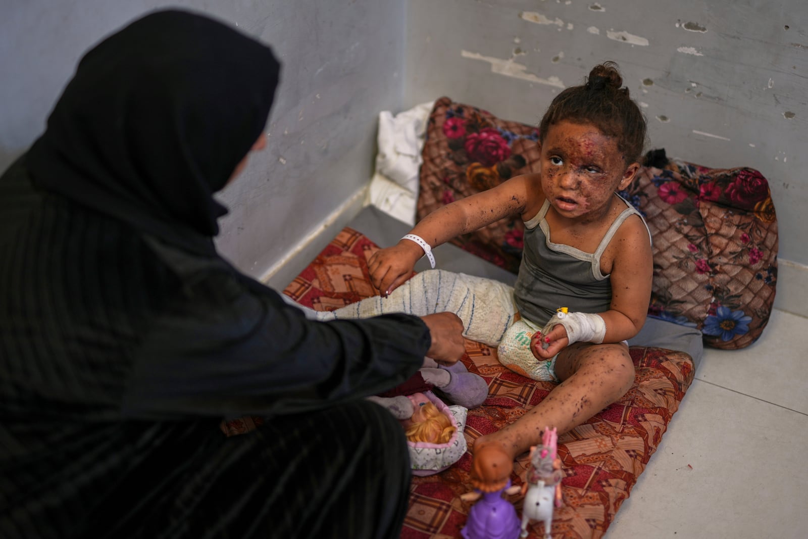 Raika Abu Sahloul, 40, cares for her 4-year-old niece, Layan, as she sits despondently among her dolls at Nasser hospital with second-degree burns on her face, foot, and stomach, caused a week earlier during an Israeli army strike on her home in Khan Younis that killed her pregnant mother and two siblings and buried her under the rubble, in Khan Younis, Gaza Strip, Sunday, May 4, 2025.(AP Photo/Abdel Kareem Hana)