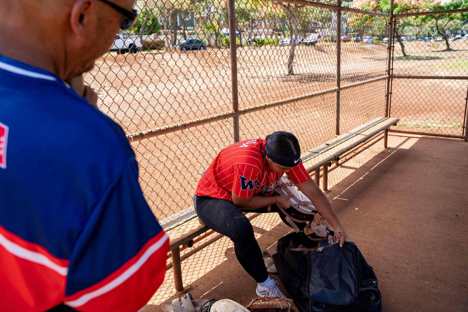 Tommy Uyeda, left, watches his daughter Ry-n, puts away her softball gear after practice, Friday, July 11, 2025, in Waianae, Hawaii. (AP Photo/Mengshin Lin)