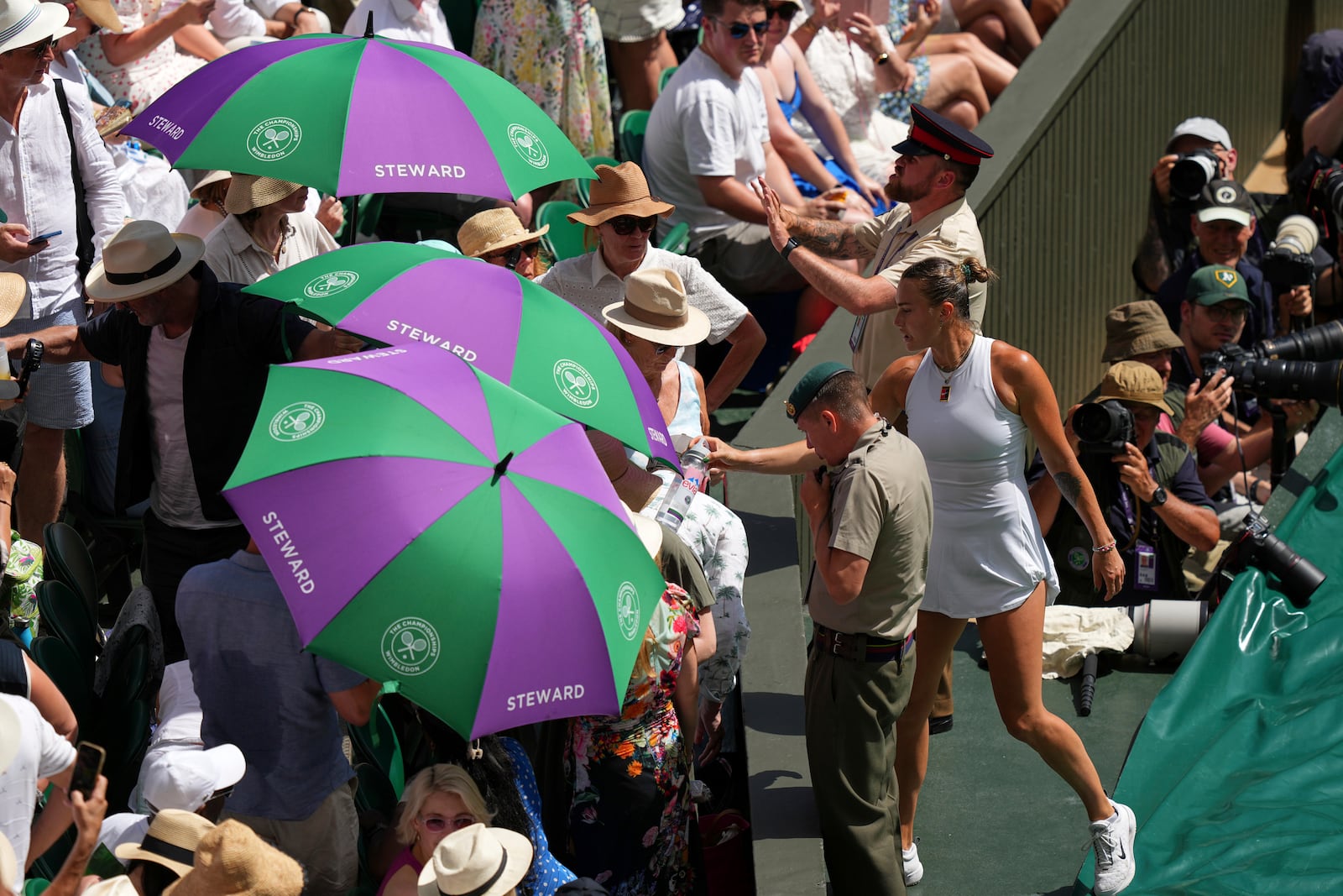 Aryna Sabalenka of Belarus, right, hands over water to be given to a member of the crowd who was overcome by the hot weather during a women's singles semifinal match against Amanda Anisimova of the U.S. at the Wimbledon Tennis Championships in London, Thursday, July 10, 2025. (AP Photo/Joanna Chan)