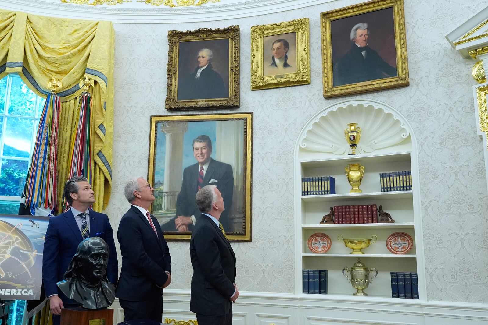 FILE - From left, Defense Secretary Pete Hegseth, Sen. Kevin Cramer, R-N.D., and Sen. Dan Sullivan, R-Alaska, look at portraits of former presidents as President Donald Trump speaks in the Oval Office of the White House, in Washington, May 20, 2025. (AP Photo/Alex Brandon, File)