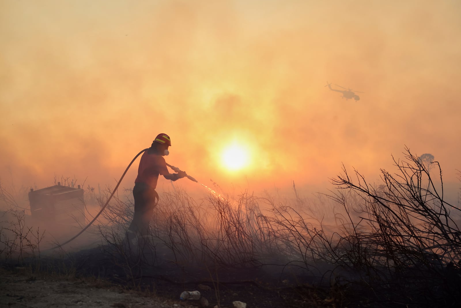 A firefighter tries to extinguish a wildfire as a helicopter flies, in the northwestern suburb of Kryoneri, in Athens, Greece, Saturday, July 26, 2025. (AP Photo/Yorgos Karahalis)