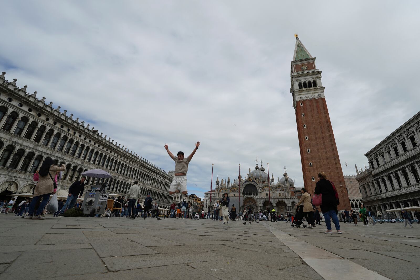 A tourist jumps in San Marco square in Venice, Italy, Friday, April 18, 2025, Venice on Friday launches for a second year a pilot program to charge day-trippers an entrance fee. (AP Photo/Antonio Calanni)