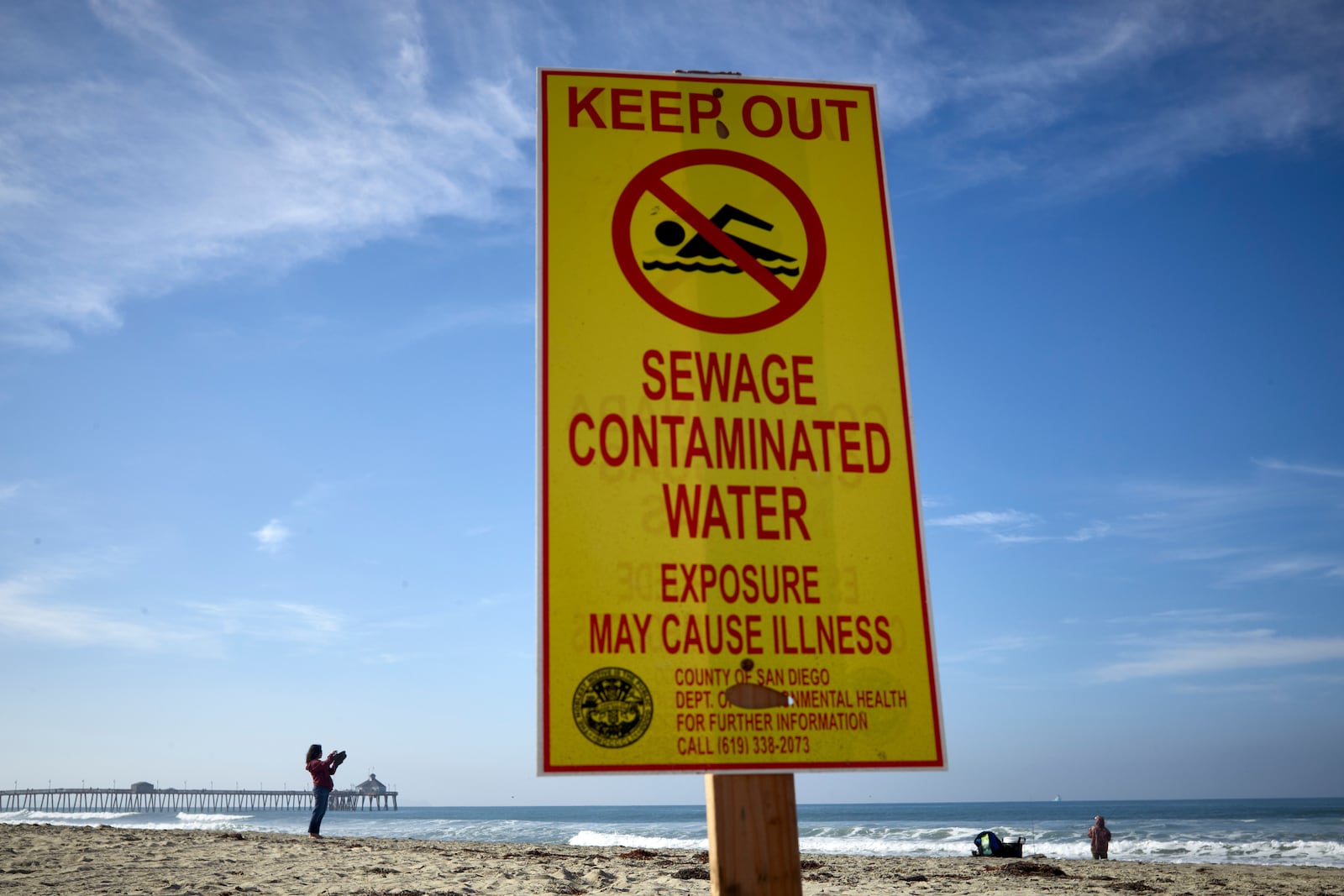 FILE - A woman records with a phone along the beach as a sign warns of contaminated water Dec. 12, 2018, at Imperial Beach, Calif. (AP Photo/Gregory Bull, File)