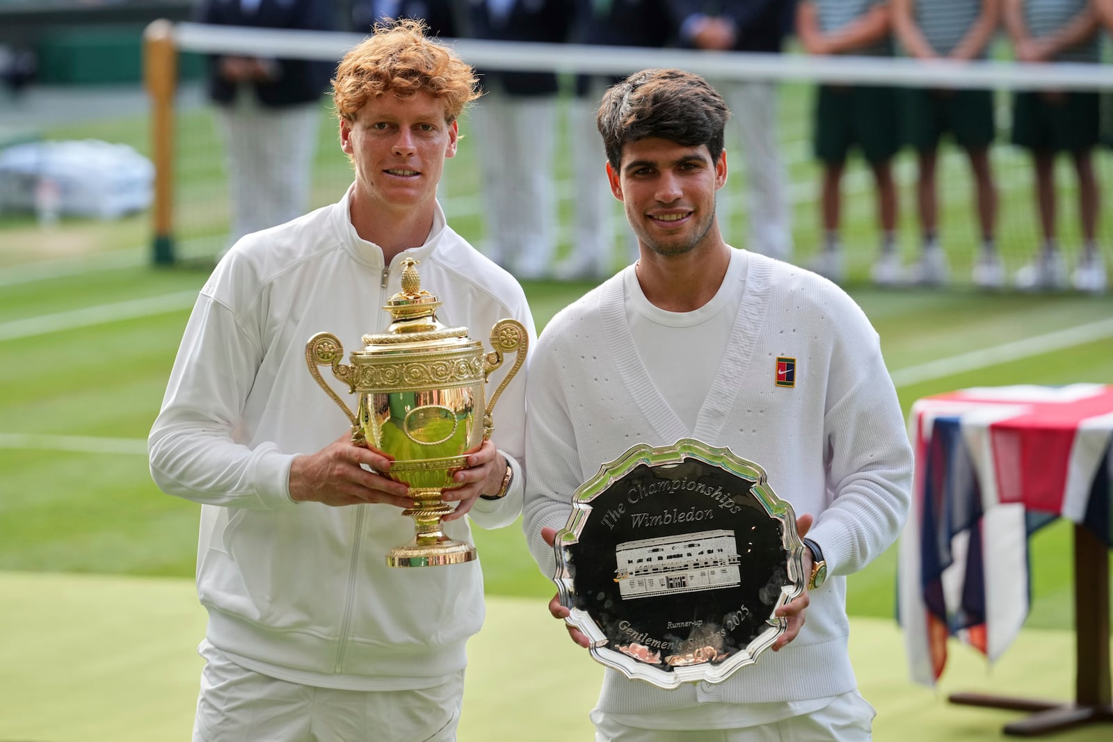 Italy's Jannik Sinner, left, celebrates with the trophy after beating Carlos Alcaraz of Spain, right, to win the men's singles final at the Wimbledon Tennis Championships in London, Sunday, July 13, 2025. (AP Photo/Kin Cheung)