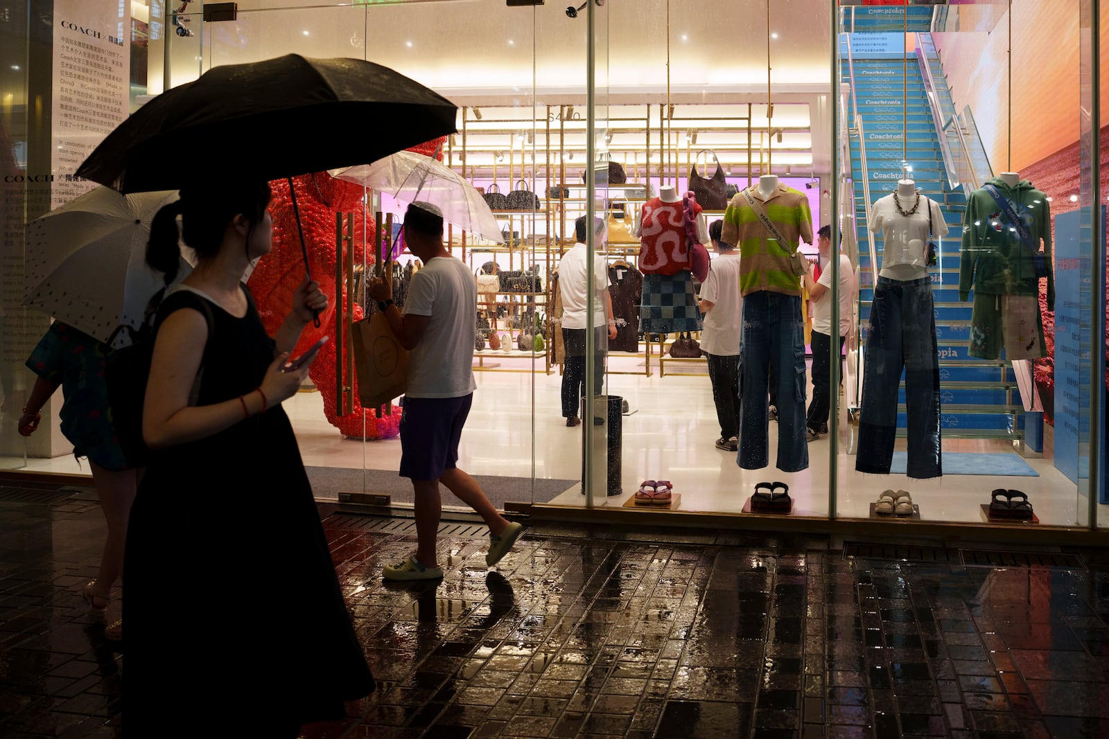 FILE - Chinese customers stroll past a clothing shop at Taikoo Li Sanlitun in Beijing, Tuesday, July, 30, 2024. (AP Photo/Vincent Thian,File)