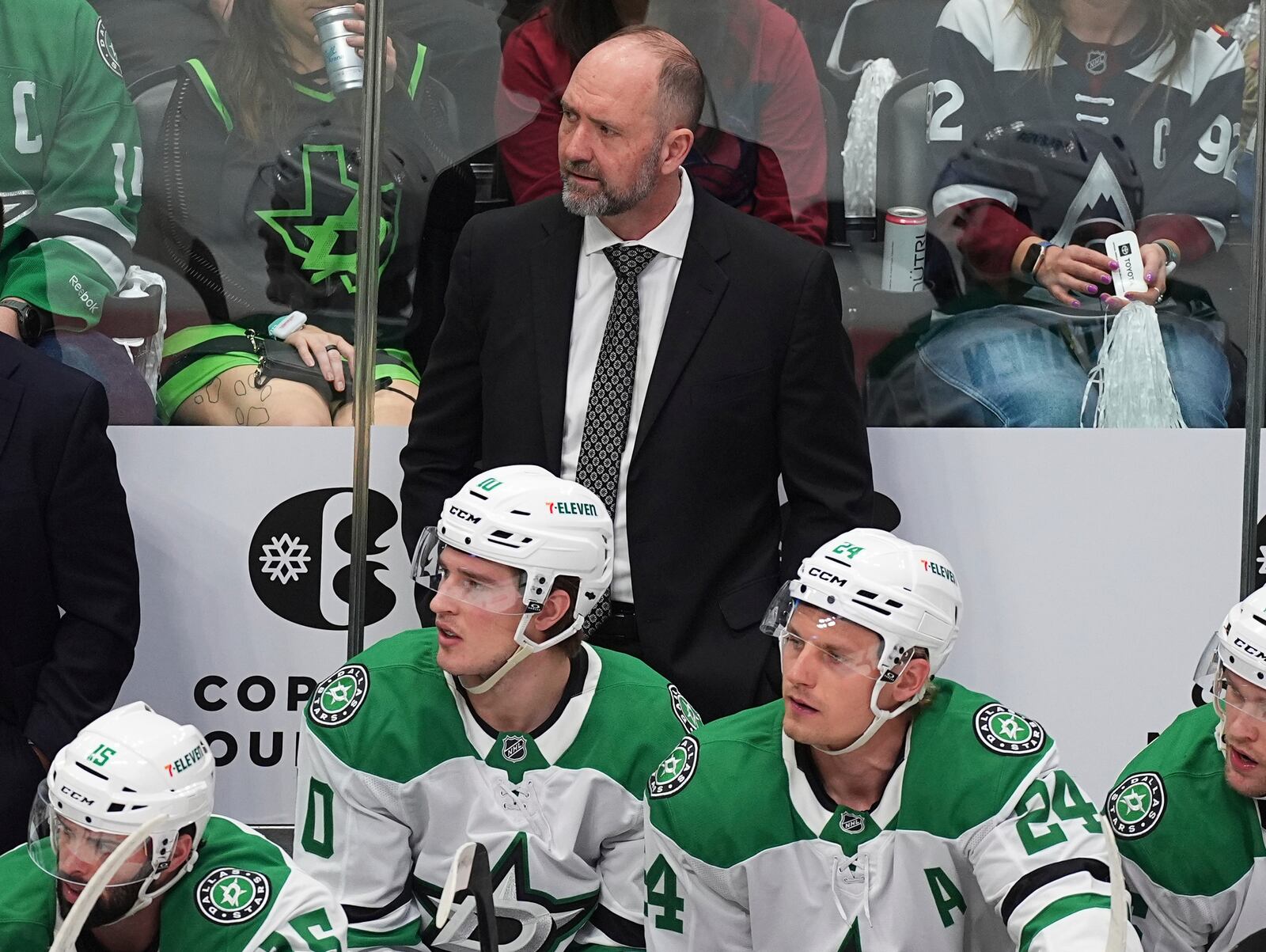 Dallas Stars head coach Peter DeBoer, back, looks on from the team box in the first period of Game 3 of an NHL hockey first-round playoff series against the Colorado Avalanche Wednesday, April 23, 2025, in Denver. (AP Photo/David Zalubowski)