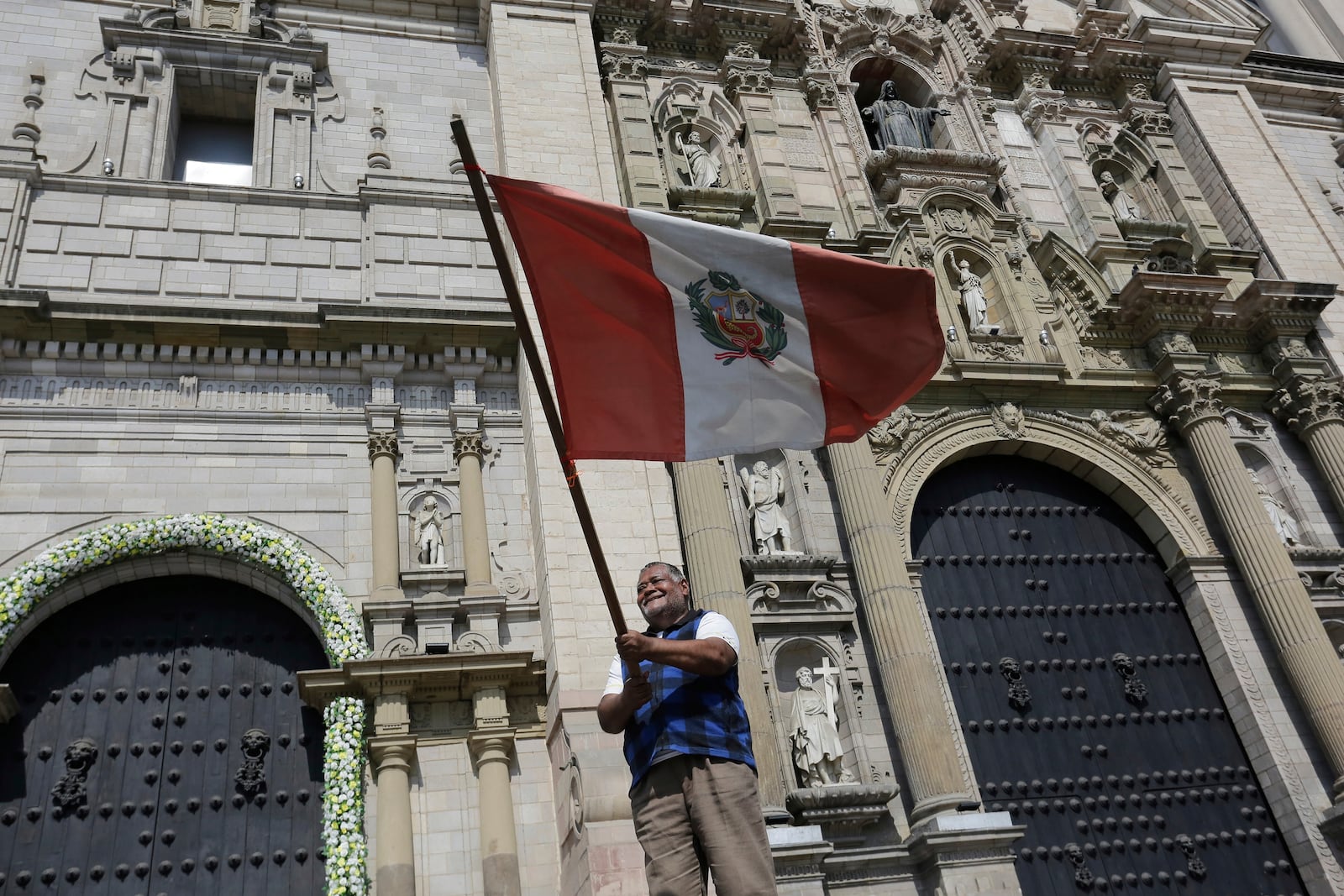 A man waves a Peruvian flag in front of the Cathedral after Cardinal Robert Prevost was elected as the new pope taking the name Leo XIV, in Lima, Peru, Thursday, May 8, 2025. (AP Photo/Cesar Zamalloa)