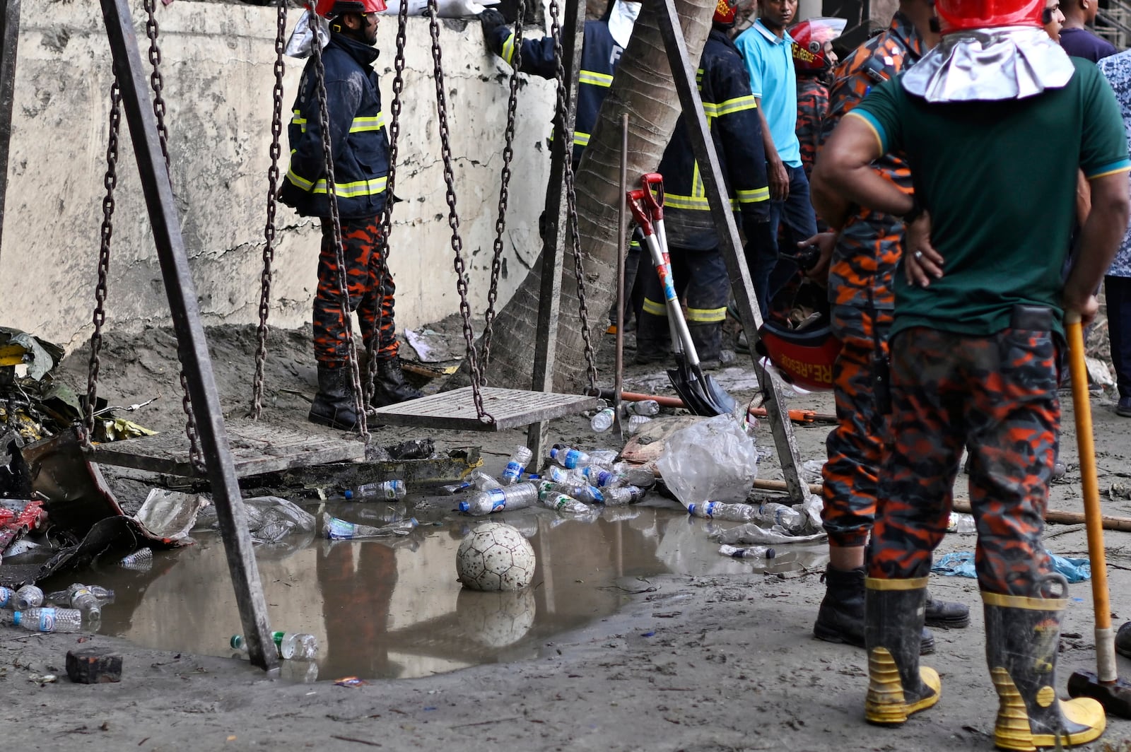 Firemen stand next to swing as they work at the site of a Bangladesh Air Force training aircraft that crashed into a school campus shortly after takeoff in Dhaka, Bangladesh, Monday, July 21, 2025. (AP Photo/Mahmud Hossain Opu)