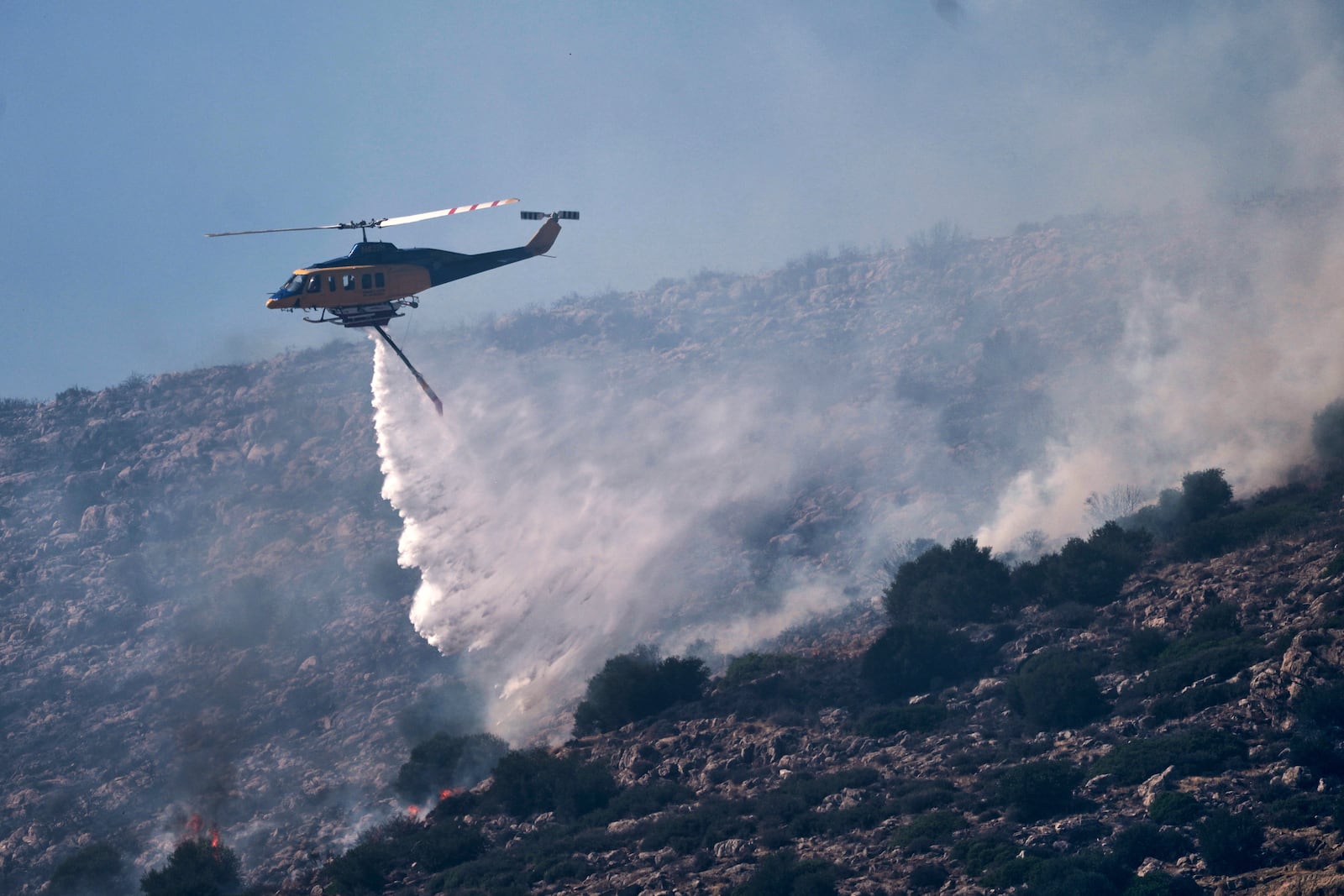 A firefighting helicopter drops water while battling a blaze in the seaside area of Palaia Fokaia, south of Athens, Thursday, June 26, 2025, as authorities evacuate five locations during Greece's first summer heatwave with temperatures nearing 40 degrees Celsius (104 Fahrenheit). (AP Photo/Thanassis Stavrakis)