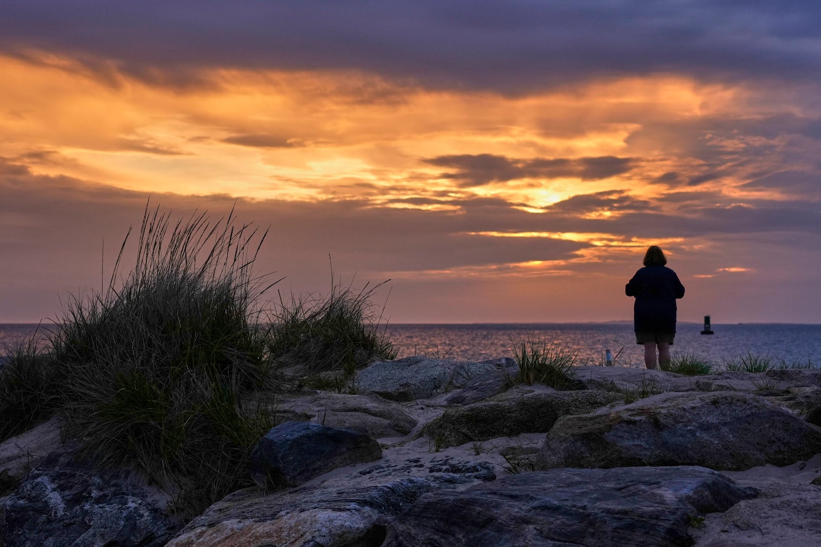 A woman views the sunset at Menemsha Beach, Wednesday, May 14, 2025, in Chilmark, Mass. (AP Photo/Robert F. Bukaty)