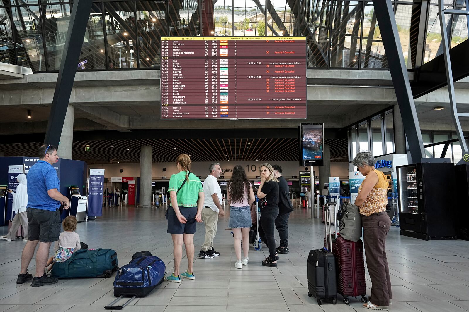 Passengers look a departures information board at Saint-Exupery airport, near Lyon, as French air traffic controllers launched a two-day strike to demand better working conditions, Friday, July 4, 2025. (AP Photo/Laurent Cipriani)