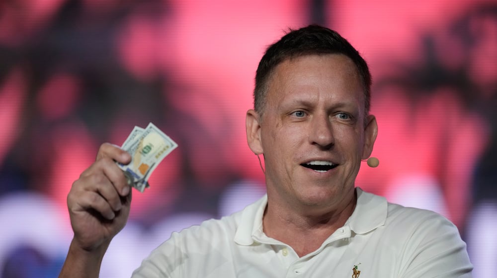 FILE - Peter Thiel, co-founder of PayPal and Palantir, offers a pair of hundred dollar bills to attendees during a keynote address at the Bitcoin Conference, April 7, 2022, in Miami Beach, Fla. (AP Photo/Rebecca Blackwell, File)