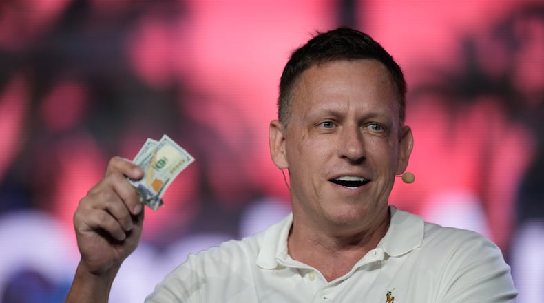 FILE - Peter Thiel, co-founder of PayPal and Palantir, offers a pair of hundred dollar bills to attendees during a keynote address at the Bitcoin Conference, April 7, 2022, in Miami Beach, Fla. (AP Photo/Rebecca Blackwell, File)