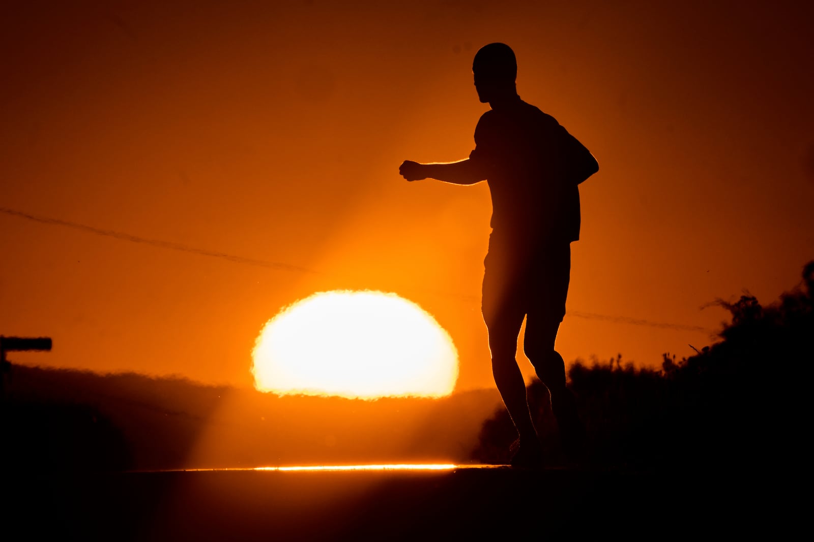 A man runs towards the rising sun on a small road on the outskirts of Frankfurt, Germany, Tuesday, July 1, 2025. (AP Photo/Michael Probst)