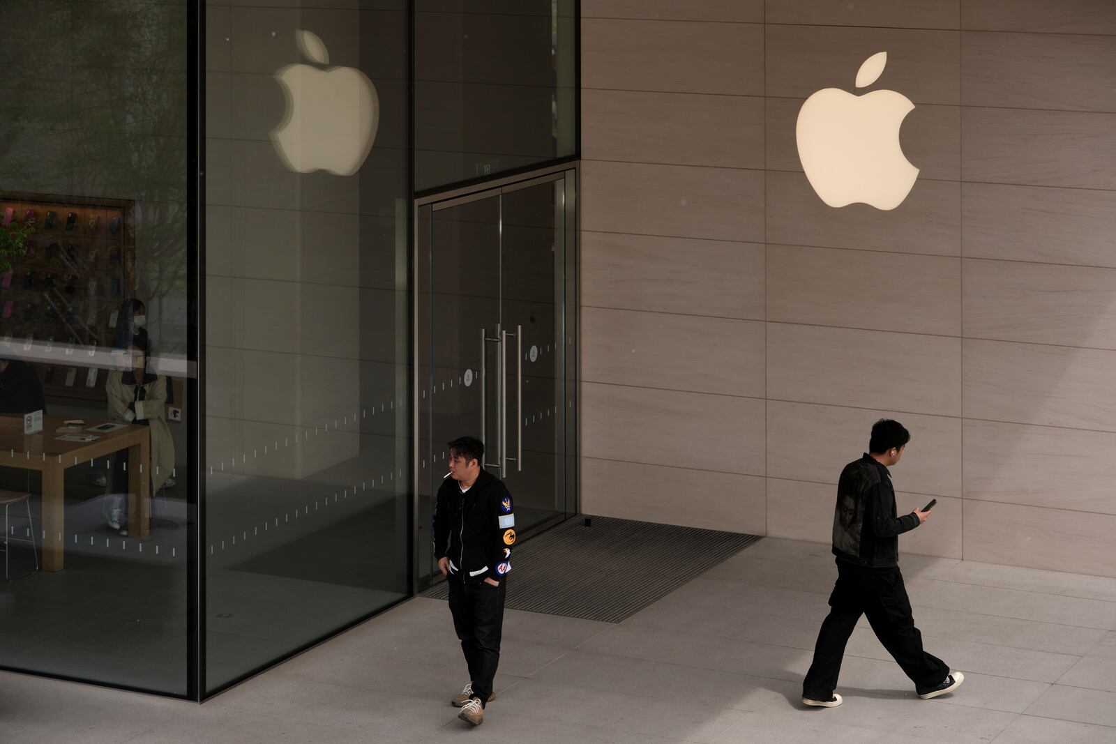 A man smokes outside an Apple Store at an outdoor shopping mall in Beijing, Tuesday, April 8, 2025. (AP Photo/Andy Wong)