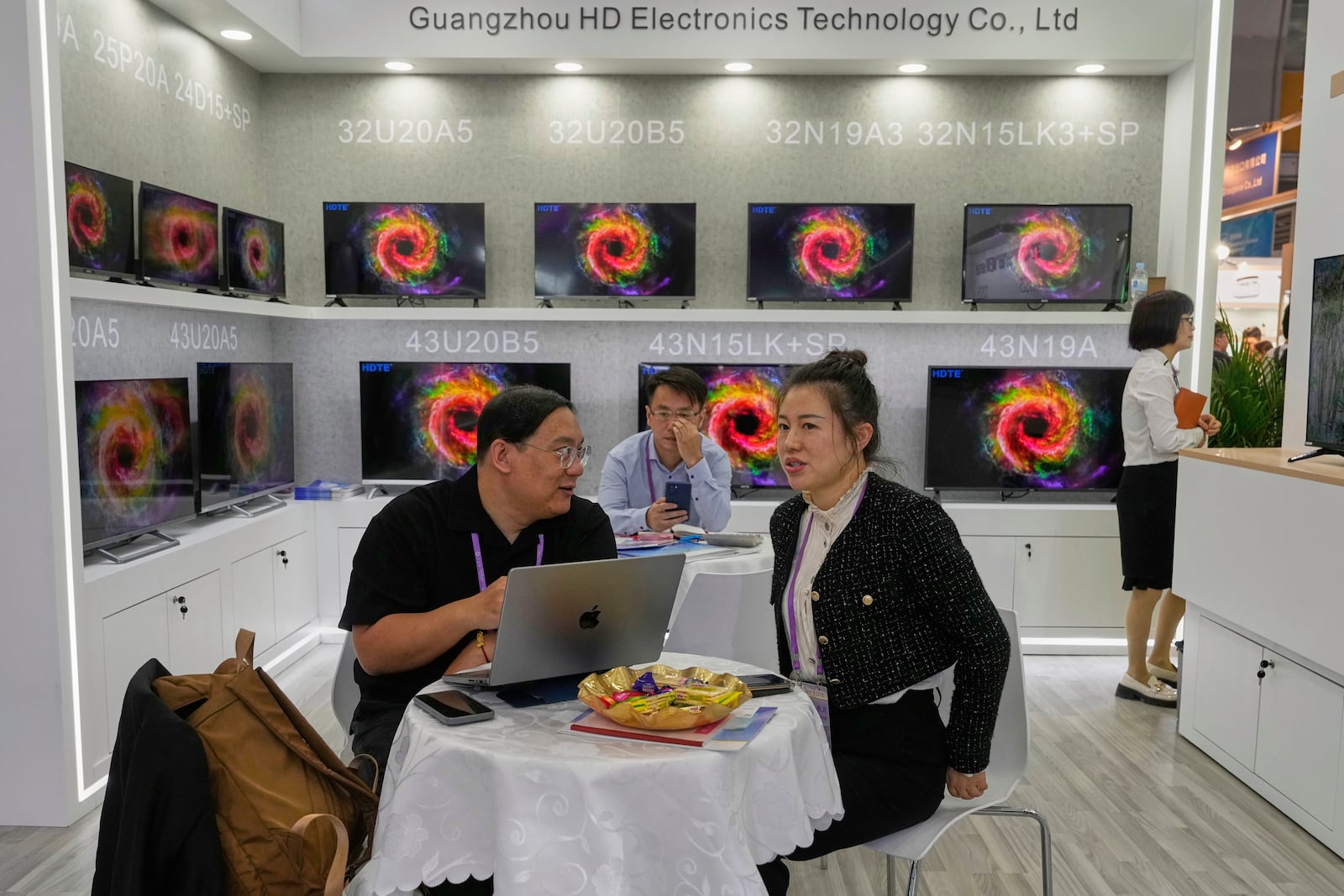 Visitors sit near television sets made by Guangzhou HD Electronics Technology Co. Ltd displayed at the 137th Canton Fair in Guangzhou, southern China's Guangdong province on Tuesday, April 15, 2025. (AP Photo/Ng Han Guan)