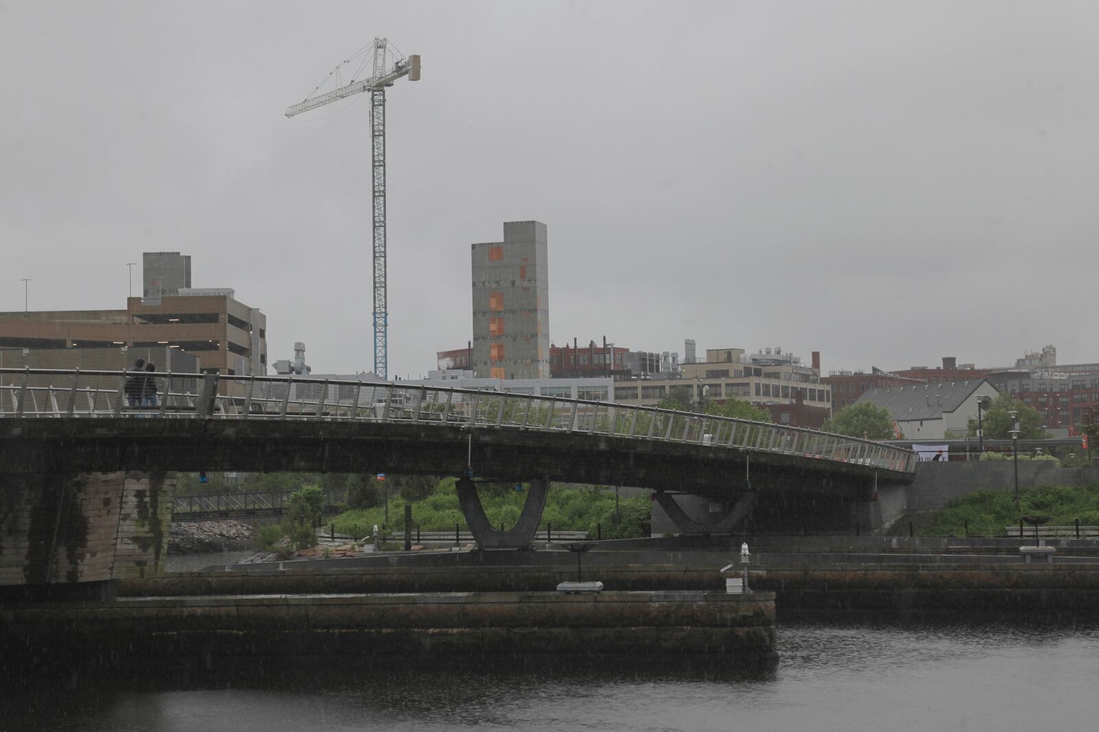 A man walks in the rain across a pedestrian bridge in Providence, R.I. on Thursday, May 22, 2025. (AP Photo/Kimberlee Kruesi)