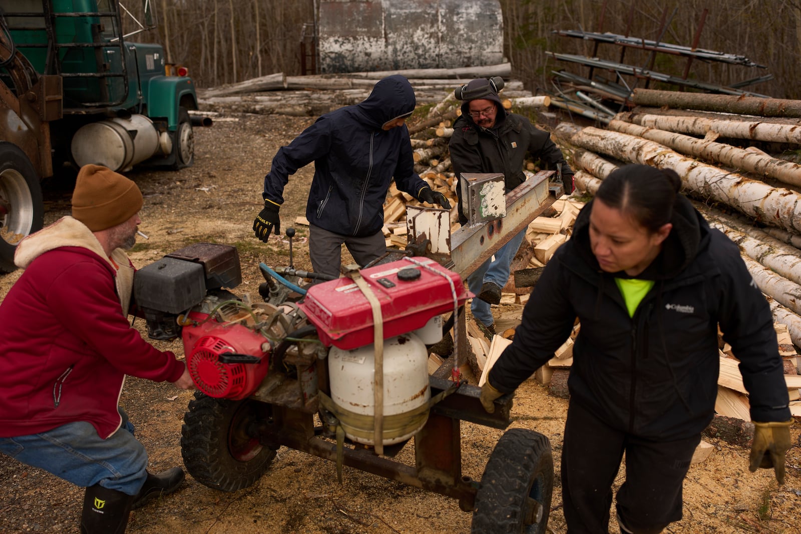 Workers with the Sustainable Energy for Galena, Alaska, from left, James Strong, Nathan Moses, Morris Demoski and Marissa McCarty move a log splitting machine before cutting wood to deliver to elders in the community Monday, May 19, 2025, in Galena. (AP Photo/John Locher)