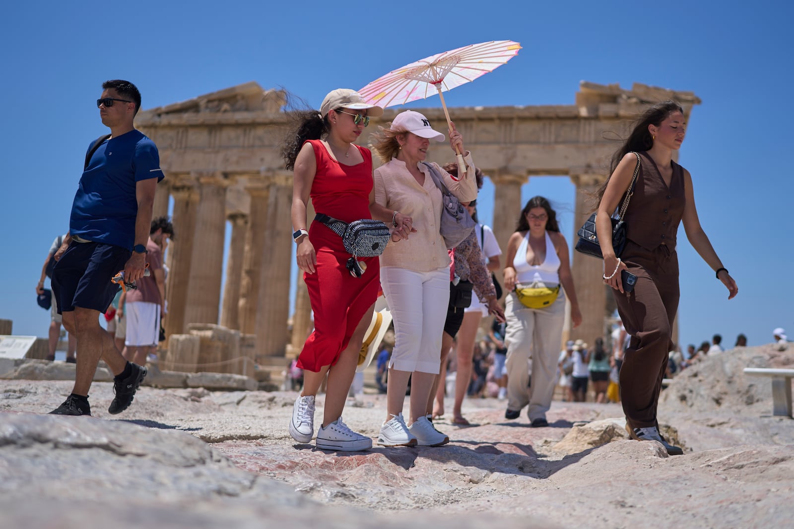 Tourists with an umbrella walk in front of the ancient Parthenon temple at the Acropolis Hill, Thursday, June 26, 2025 as the summer's first heatwave hits Greece, with temperatures expected to edge over 40 degrees Celsius, (104 Farenheit).(AP Photo/Petros Giannakouris)