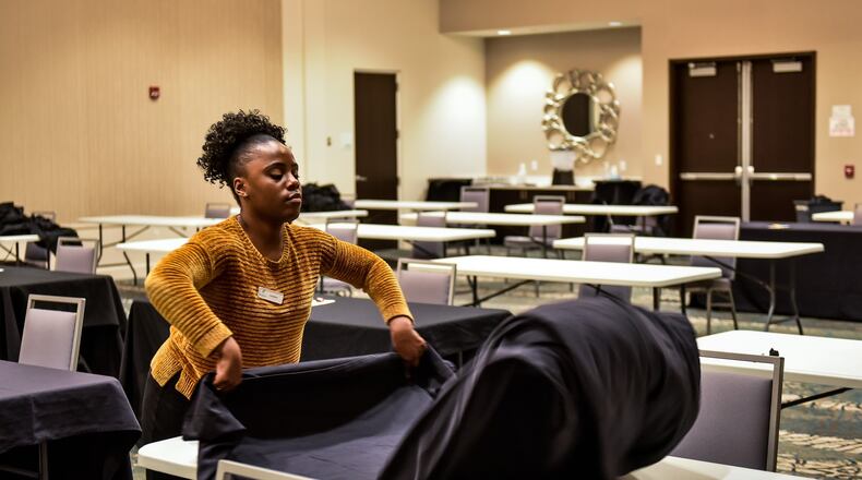Hannah Johnson, wedding sales manager at Centre Park of West Chester Event & Banquet Center, at the Holiday Inn on Mulhauser Road in West Chester Township replaces tablecloths on tables spaced apart with single chairs at each table in one of the event spaces Thursday, March 26, 2020. A company is using the space for training during the coronavirus pandemic. The banquet space that would normally hold around 100 people is spaces apart so only about 30 people can use the room. NICK GRAHAM / STAFF