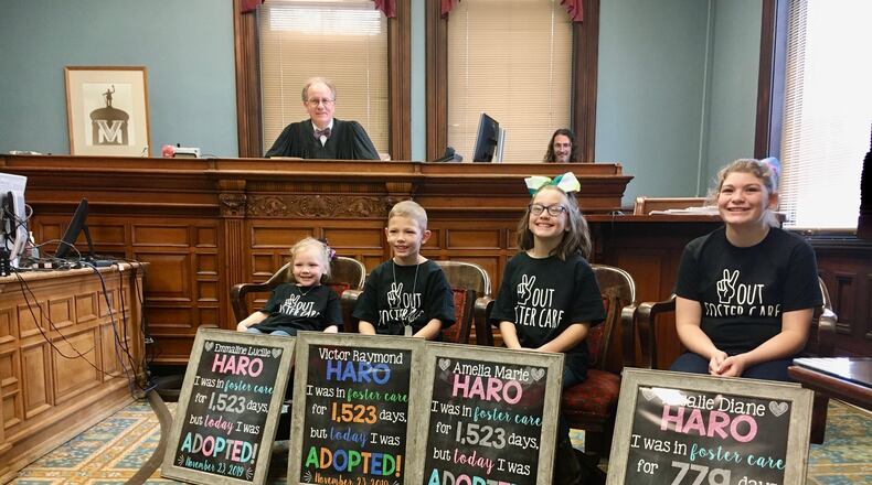 Four formally foster children of the Haro family proudly display their homemade signs - as presiding Butler County Common Pleas Probate Judge Randy Rogers looks on from bench - noting their days in in the foster system. Rogers granted the legal adoption Saturday of (L-R) 4-year-old Emmaline Haro; 8-year-old Victor; 9-year-old Amelia and 13-year-old Rosalie Hora to their new mother and father, Dani and Matt Haro. (Photo By Michael D. Clark/Journal-News)