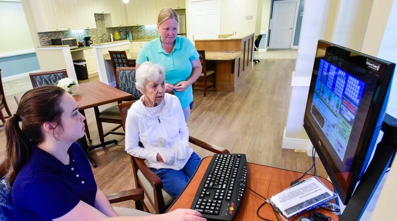 Natalee Downard, left, and Kristin Wilson, standing, play a word scramble game with resident, Gayle Pope in the Pope Dining Room, named in honor of Gayle Pope who is the first resident of Thrive Memory Care now open on Heritagespring Drive in Liberty Township. The Alzheimer’s and memory loss care facility offers full service memory care for residents. NICK GRAHAM/STAFF