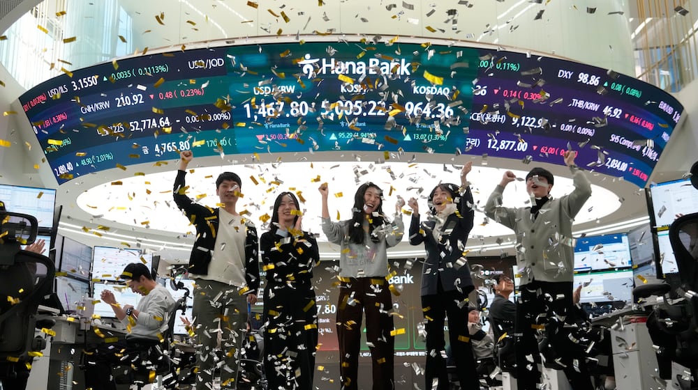 Currency traders celebrate as they work in the office with a screen showing the Korea Composite Stock Price Index (KOSPI), center top, of over 5,000 points at the foreign exchange dealing room of the Hana Bank headquarters in Seoul, South Korea, Thursday, Jan. 22, 2026. (AP Photo/Ahn Young-joon)