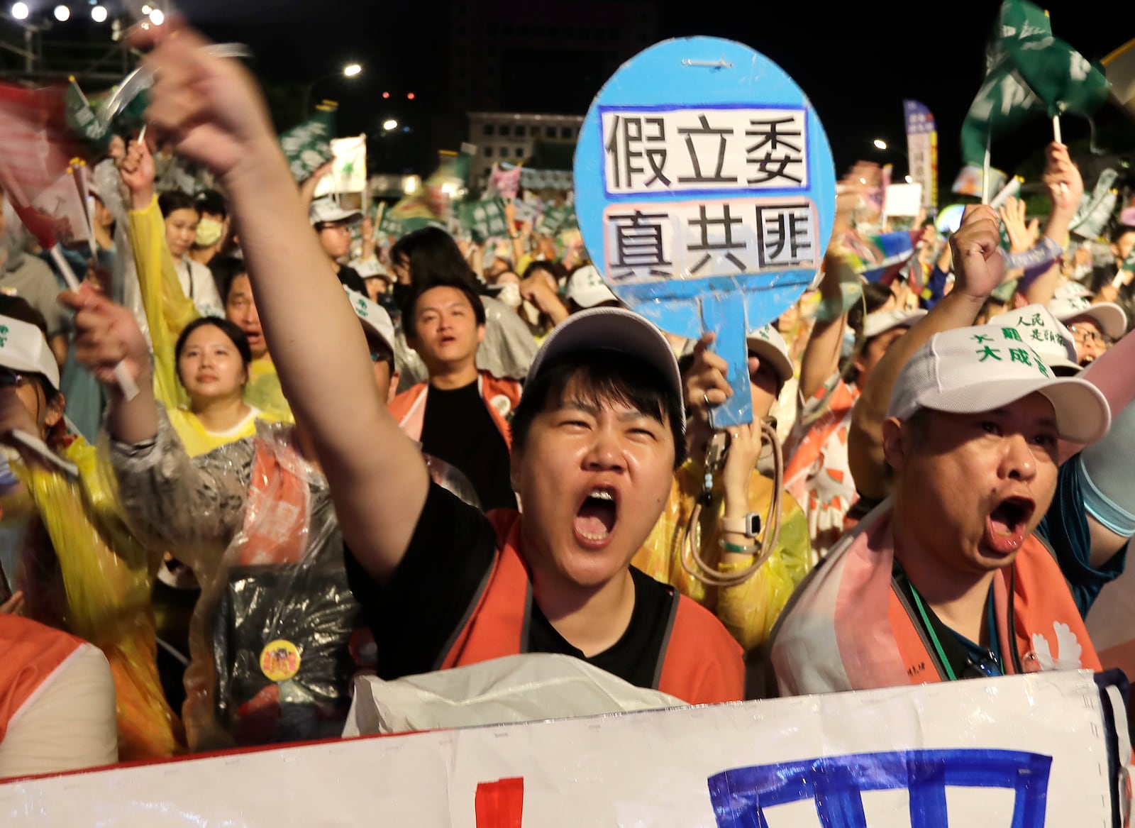 People shoot behind a slogan reading ''Fake Legislators Are Real Communist Bandits'' during a campaign rally to promote recall vote targeting 24 Nationalist Party (KMT) lawmakers in Taipei, Taiwan, Thursday, July 24, 2025. (AP Photo/Chiang Ying-ying)