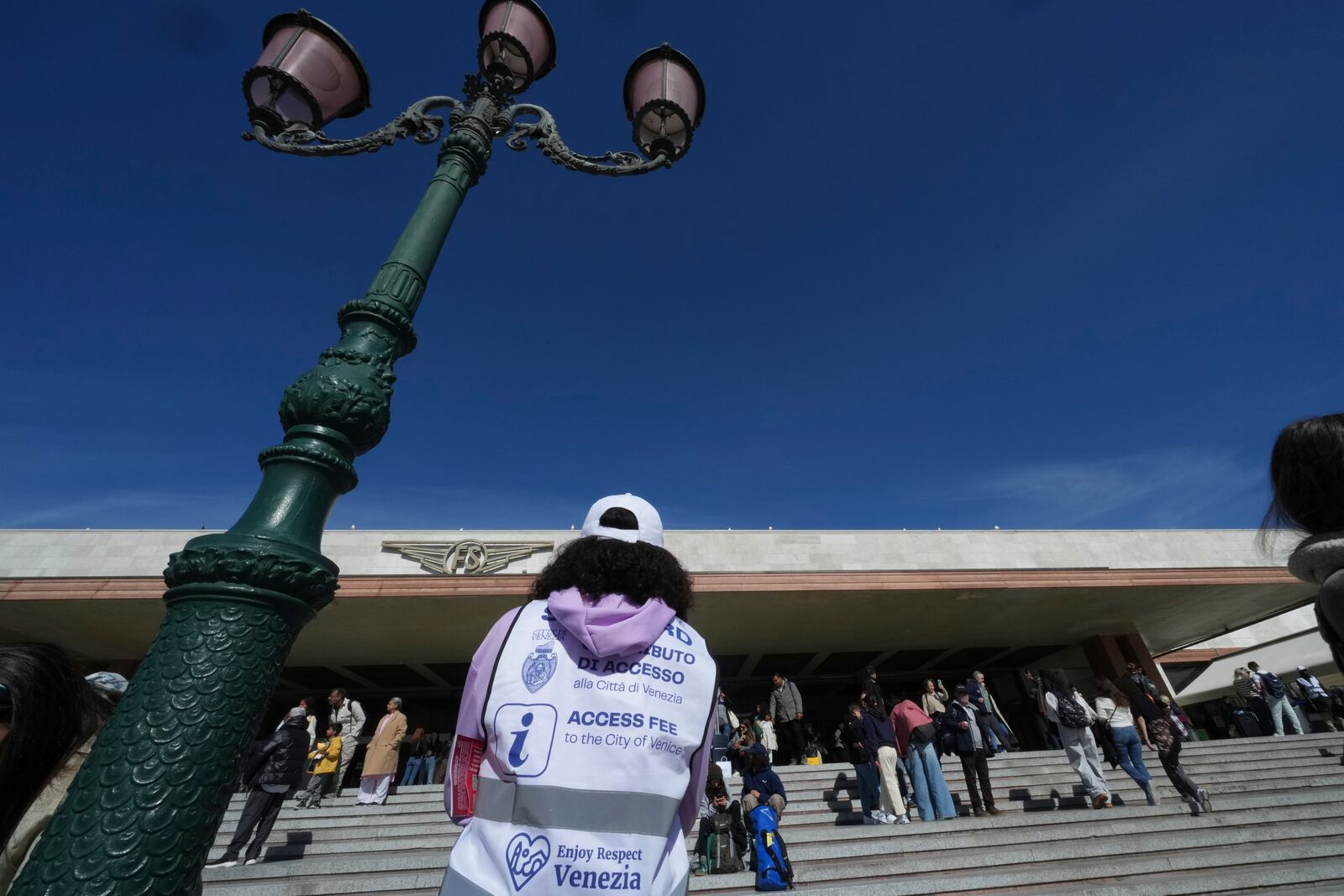Stewards check tourists' QR codes outside the main train station in Venice, Italy, Friday, April 18, 2025, as the city for a second year is charging day-trippers an arrivals tax. (AP Photo/Antonio Calanni)