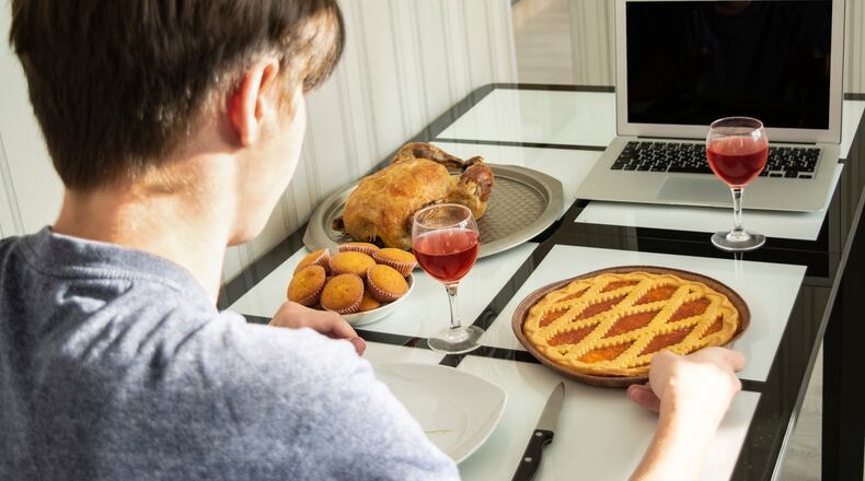 Back view of a self-isolating young man arranging a festive Thanksgiving feast online via video call.