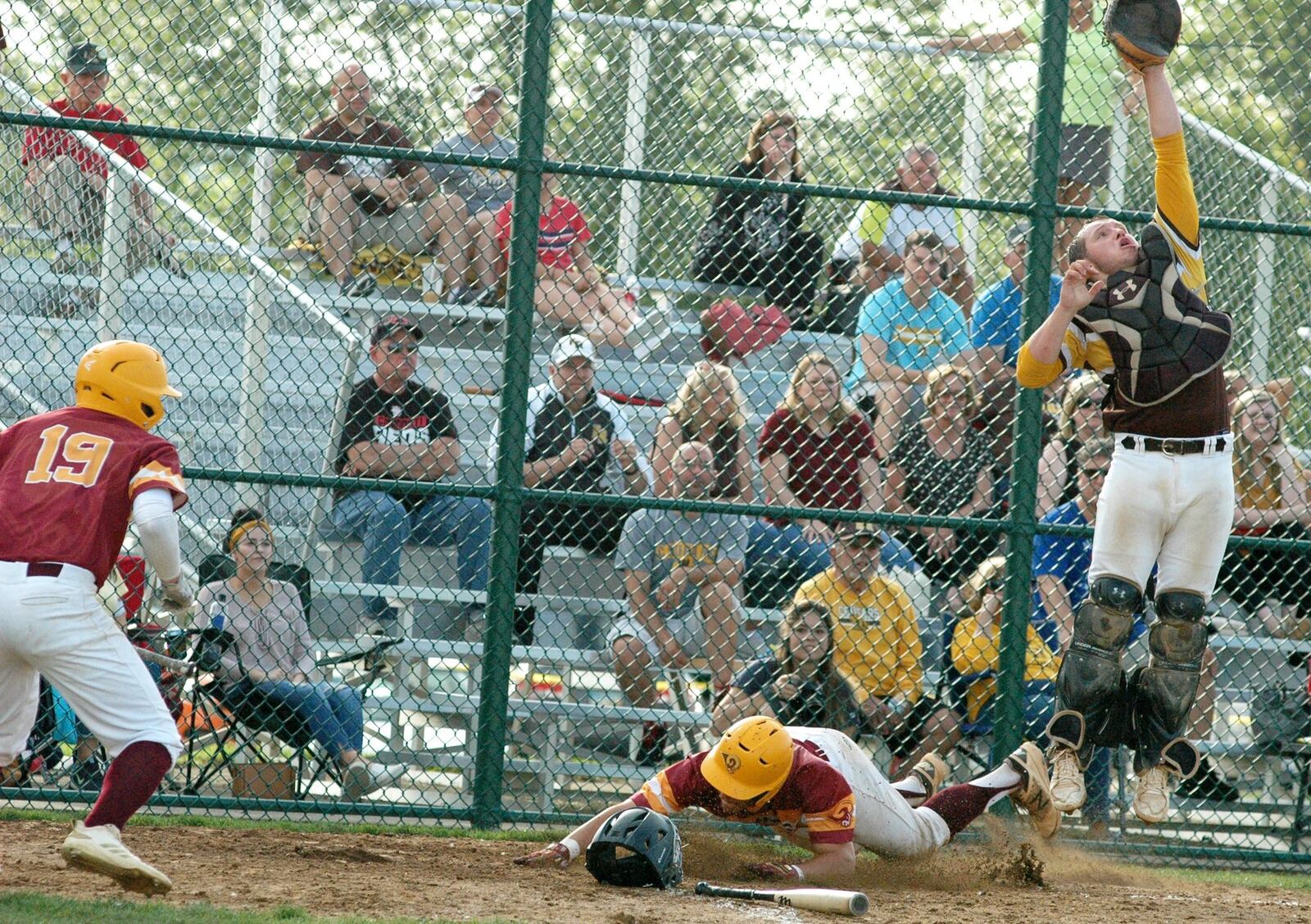 Springfield Kenton Ridge catcher Kaelan Lemen goes high for the throw as Keegan Nickoson of Ross scores the winning run in the bottom of the seventh inning Thursday during a Division II district baseball final at Hamilton’s Stang Field. That’s the Rams’ Eric Guckiean (19) with a front-row view of the play. Ross won 1-0. RICK CASSANO/STAFF