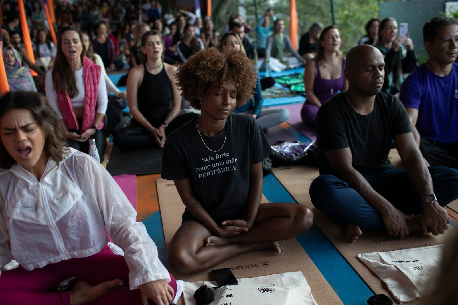 A woman sitting in the lotus position wears a shirt that reads in Portuguese, "Be strong like a like a mother from the outskirts" while meditating during a Transformation Project yoga class in the Rocinha favela, in Rio de Janeiro, Wednesday, July 9, 2025. (AP Photo/Bruna Prado)
