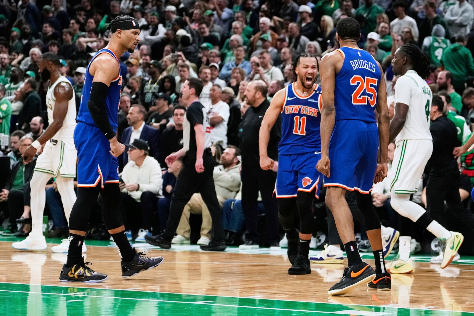New York Knicks guard Jalen Brunson (11) celebrates after a win with teammates as Boston Celtics' Jrue Holiday, right, and Jaylen Brown, back left, walk off the court following Game 1 of an NBA basketball second-round playoff series Monday, May 5, 2025, in Boston. (AP Photo/Charles Krupa)