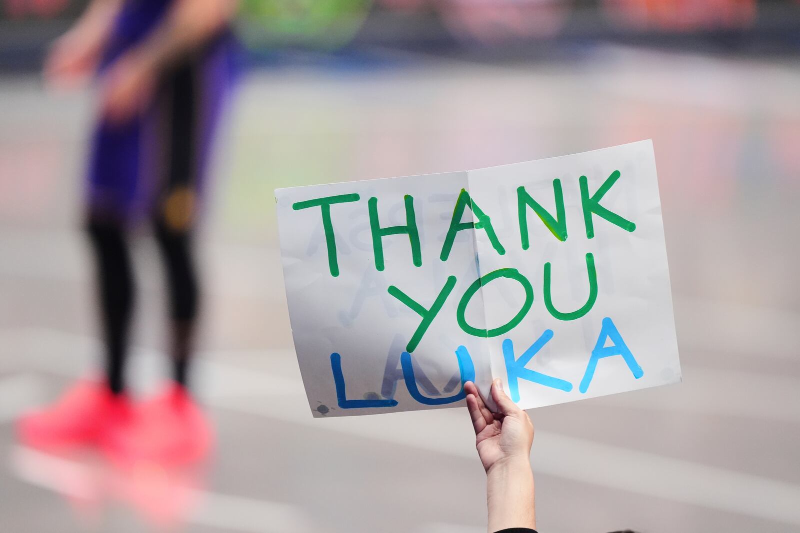A fan holds up a sign thanking Los Angeles Lakers' Luka Doncic as he stands on the court at rear late in the second half of an NBA basketball game against the Dallas Mavericks in Dallas, Wednesday, April 9, 2025. (AP Photo/LM Otero)
