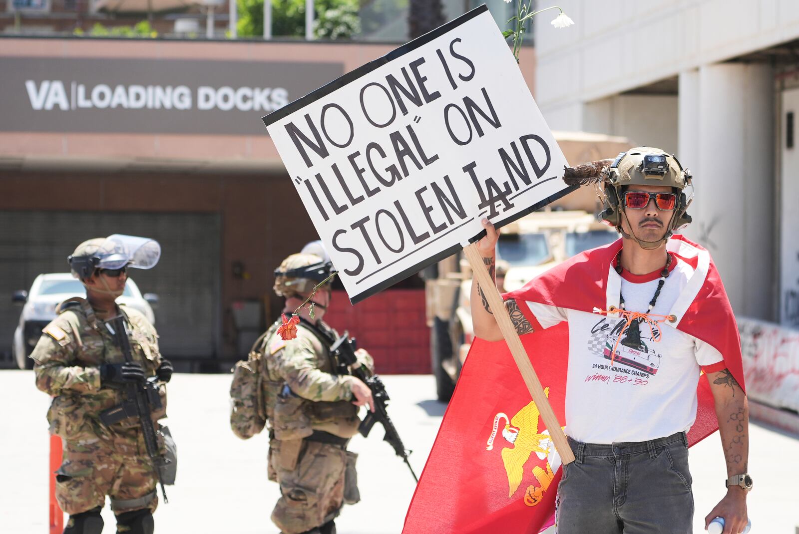 Jack Murillo, a Marine veteran, holds a sign in front of law enforcement guarding a federal building on Tuesday, June 17, 2025, in Los Angeles. (AP Photo/Damian Dovarganes)
