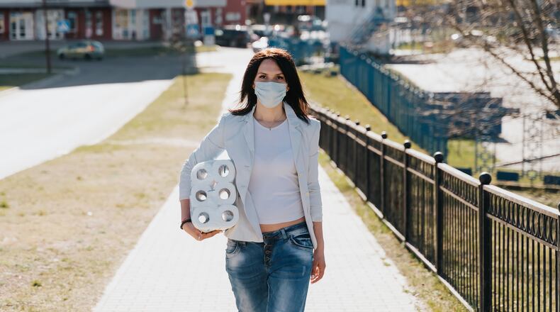 Woman walking in medical mask with toilet paper during coronavirus outbreak or covid-19. concept of covid-2019 quarantine. (Source: Shutterstock)