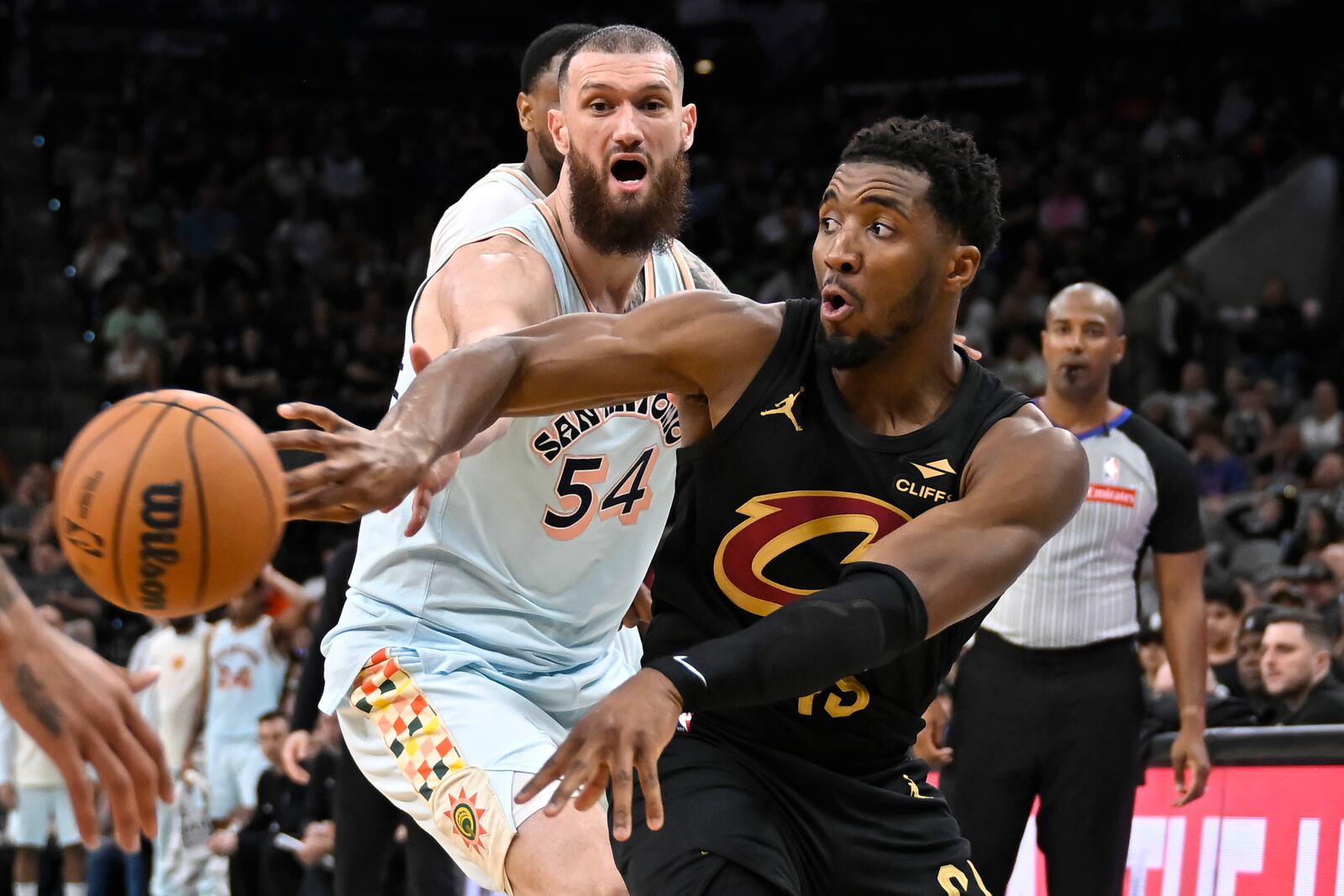 Cleveland Cavaliers guard Donovan Mitchell, right, passes the ball as he is guarded by San Antonio Spurs forward Sandro Mamukelashvili (54) during the second half of an NBA basketball game, Friday, April 4, 2025, in San Antonio. (AP Photo/Darren Abate)