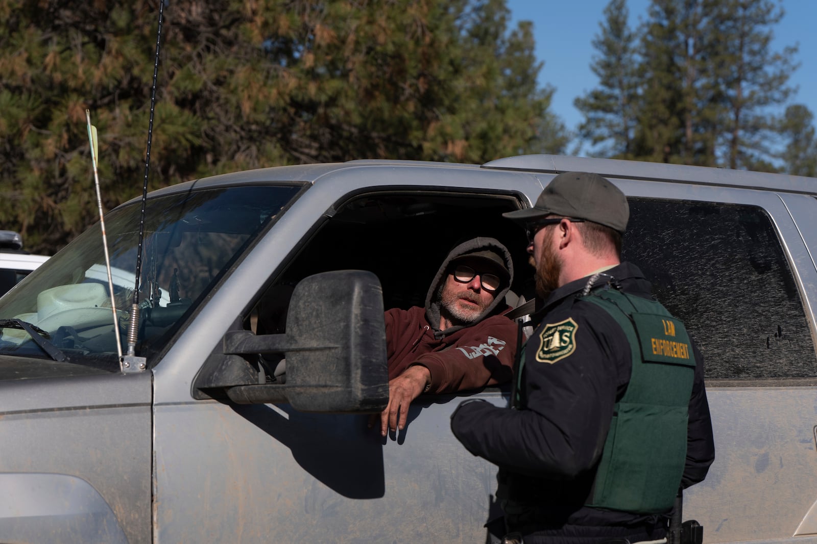 A person talks to a U.S. Forest Service official about getting through a road barrier to collect their belongings at a homeless encampment in Deschutes National Forest, Thursday, May 1, 2025, near Bend, Ore. (AP Photo/Jenny Kane)