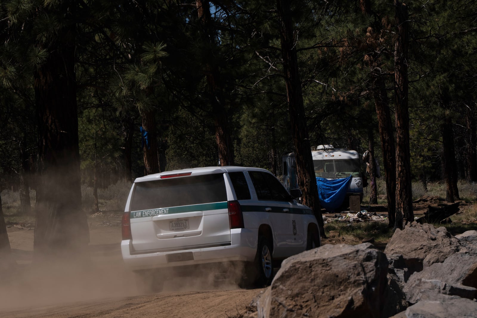 A U.S. Forest Service vehicle drives down a dirt road past newly placed rock barrier towards a trailer at a homeless encampment in Deschutes National Forest, Thursday, May 1, 2025, near Bend, Ore. (AP Photo/Jenny Kane)