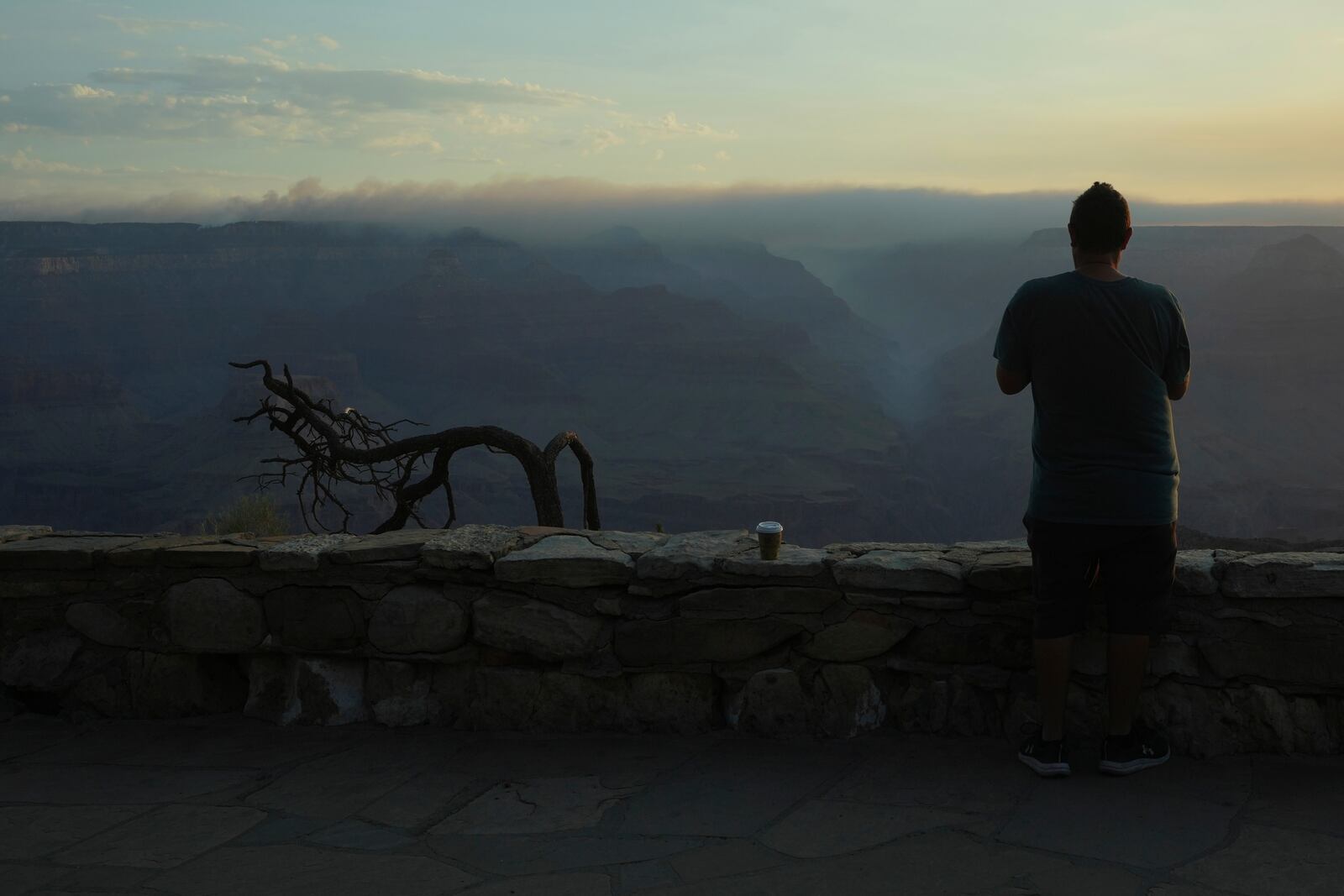 A tourist watches from a South Rim overlook as the early morning smoke from the Dragon Bravo Fire moves over the Grand Canyon from the North Rim Tuesday, July 15, 2025, in Grand Canyon National Park, Ariz. (AP Photo/Ross D. Franklin)